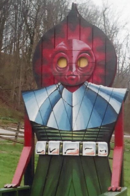 A commemorative chair from Flatwoods, WV meant to depict the Flatwoods Monster. The figure has a red head with large yellow eyes, a silver color, and green body.